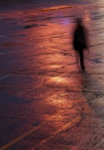 Unrecognised person walking alone in the dark under bright orange light after rain