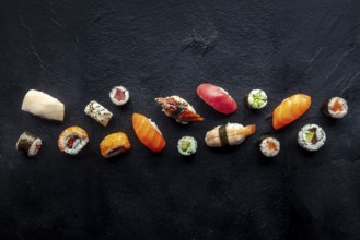 Sushi overhead flat lay shot. Rolls, maki, nigiri on a black slate background, Japanese food.