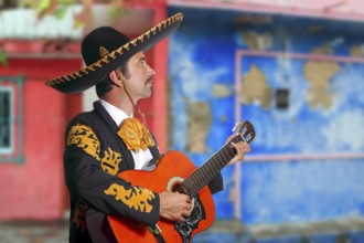 Charro Mariachi singer playing guitar in Mexico houses background