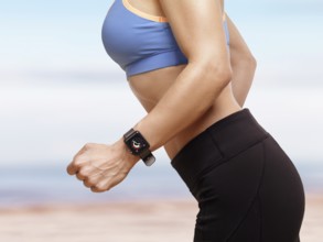 Woman jogging outdoors at the beach with Apple Watch smartwatch on her wrist displaying daily
