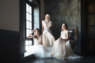 Three young women near window wearing wedding dresses