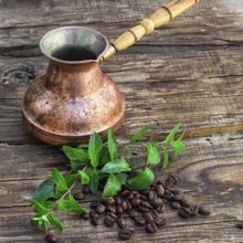 Vintage copper Turk on wooden background covered coffee beans with mint petals
