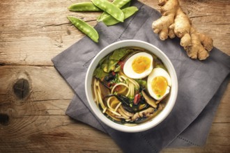 Miso soup with noodles, nori seaweed, snow peas, ginger and an egg in a bowl on a rustic wooden