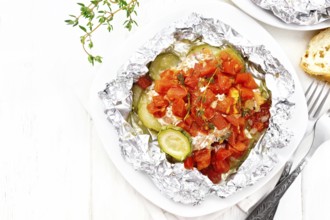 Pink salmon with zucchini, tomatoes, onions, garlic and thyme, baked in foil on a plate, napkin,