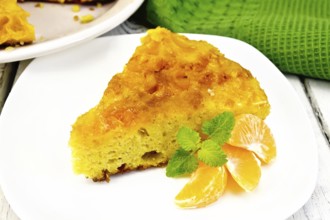 Piece of tart with mandarin, mint, mandarin slices in a white plate, towel on a background of