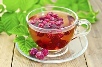 Tea with raspberries in a glass cup, green raspberry leaves on the background of wooden boards