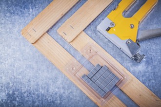 Collection of stapler gun metal staples wooden building board on metallic background