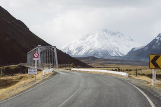 Road leading to a bridge with snow-capped mountains and cloudy sky in the background, Hooker Valley