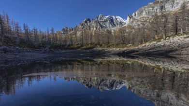A tranquil mountain lake reflects the surrounding snow-capped mountains and clear blue sky, Lago