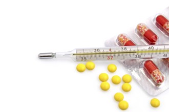 Thermometer with the yellow pills in bulk and red-white capsules in a package on a white