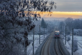 Passenger train traveling on railway tracks through frozen trees, at sunrise, in the German