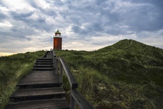 Evening landscape with wooden stairs over marram grass hill, toward red lighthouse, on Sylt island,