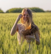 Portrait of a laughing girl with matted hair in a wheat field at sunset