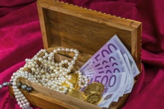 Gold in coins and bars with jewellery on red velvet. Symbolic photo for wealth, luxury, wealth tax.
