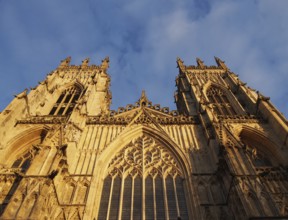A front view of the towers at the entrance to york minster in sunlight against a blue cloudy sky