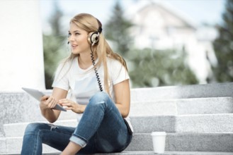 Happy young woman with vintage headphones and a cup of coffee to go, surfing the internet on a