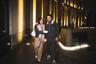 Couple walking and conversing at night in a city with lit architectural surroundings