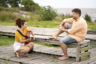 Women squatting playing guitar for her boyfriend in a park near the sea