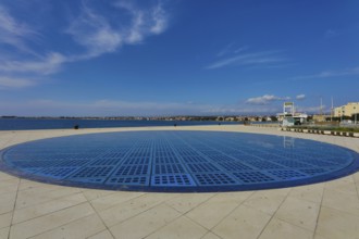 Modern circular solar installation by the sea with clear sky and calm surroundings, artwork