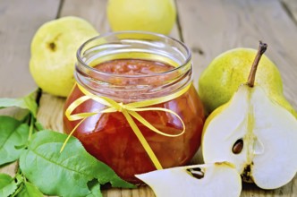 Pear jam in a glass jar, fresh pears, twigs with leaves on a wooden board