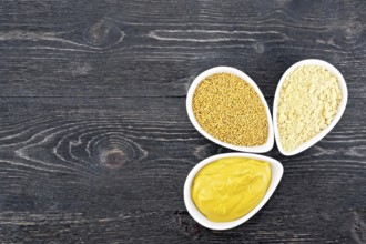 Mustard sauce, seeds and mustard powder in three saucepans on a wooden plank background