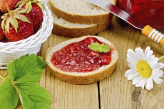 Bread with strawberry jam, a jar of jam, knife, strawberries in a wicker basket, chamomile on a