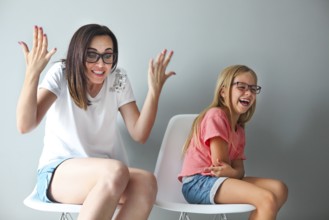 Happy mother and her little daughter sitting on the chairs by the grey wall. Portrait of mother and