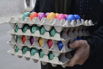 Person holding several stacks of coloured eggs for Easter