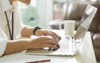 Businessman using laptop with tablet and pen on white table in office with a cup of coffee, side