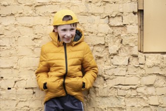 A child on the street A cheerful boy in yellow clothes and a baseball cap stands against a brick