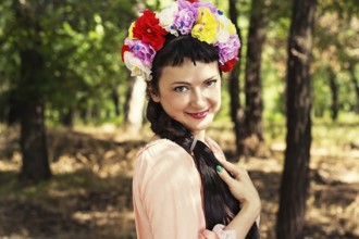 Charming woman in wreath of roses on her head on the background of nature