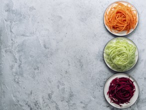 Vegetable noodles - zucchini, carrot, and beetroot noodles on plate over gray cement background.