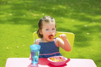 Toddler kid girl eating macaroni tomato pasta in garden turf grass