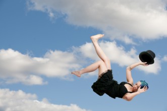 A beautiful young actress dancer wearing a top hat flying through the sky or falling through the