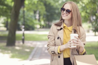 Young fashionable woman taking a coffee break after shopping and walking with a coffee to go in her