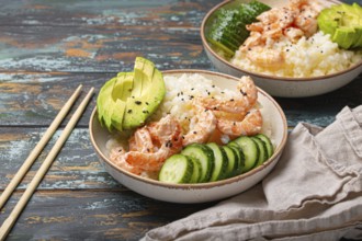 White ceramic bowl with rice, shrimps, avocado, vegetables and sesame seeds and chopsticks on