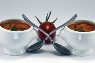 Cream of tomato soup in a white bowl with a spoon and a cherry tomato