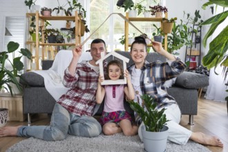 Traditional family with child are enjoying new home, sitting on the sofa and holding the roof.