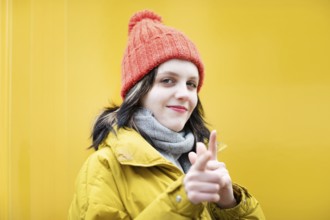 Woman with red hat pointing with fingers in front of yellow background, positive expression