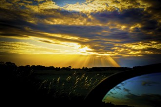 A dramatic sunset with yellow and blue tones, rays of light through clouds and a dark silhouette in