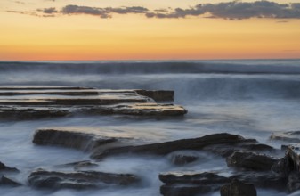 Dramatic beautiful sunset on a rocky coast with waves crashing on the rocks at Akrotiri area in