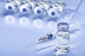 Single use syringe for injection treatment on medical table with vials of liquid drug doses flu