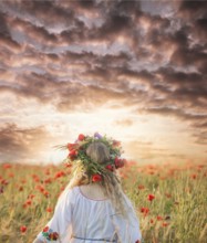 Pretty blonde girl in a dress with a pattern poppy and with a wreath on his head enjoying in a