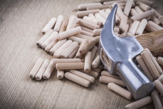 Dowel pins and claw hammer on wooden board construction concept