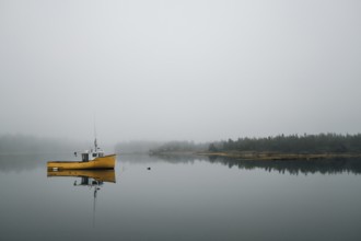 A commercial fishing boat is reflected in the still calm water of a protected bay as light fog