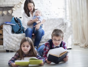Son and daughter with their mother and little brother siting on the sofa. Children readind books in