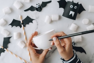 Female hands paint on white cup scary jacks face DIY for kids Halloween home activities Holiday art