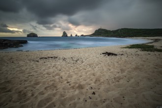 A secluded bay with a sandy beach in the morning. At the end of the beach a pointed rock formation