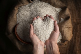 Human hands in shape of heart holding handful of rice over burlap sack