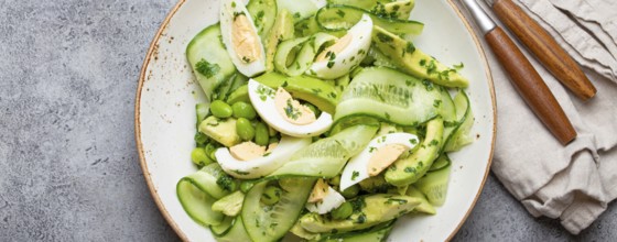 Healthy green avocado salad bowl with boiled eggs, sliced cucumbers, edamame beans, olive oil and